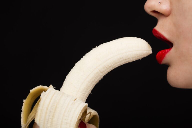 Woman with Red Lipstick Eating Banana on Black Background