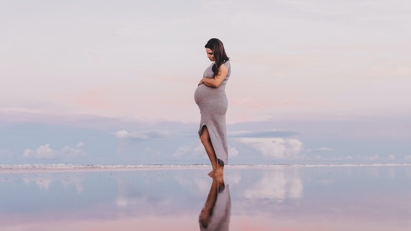 pregnant woman standing on calm body of water