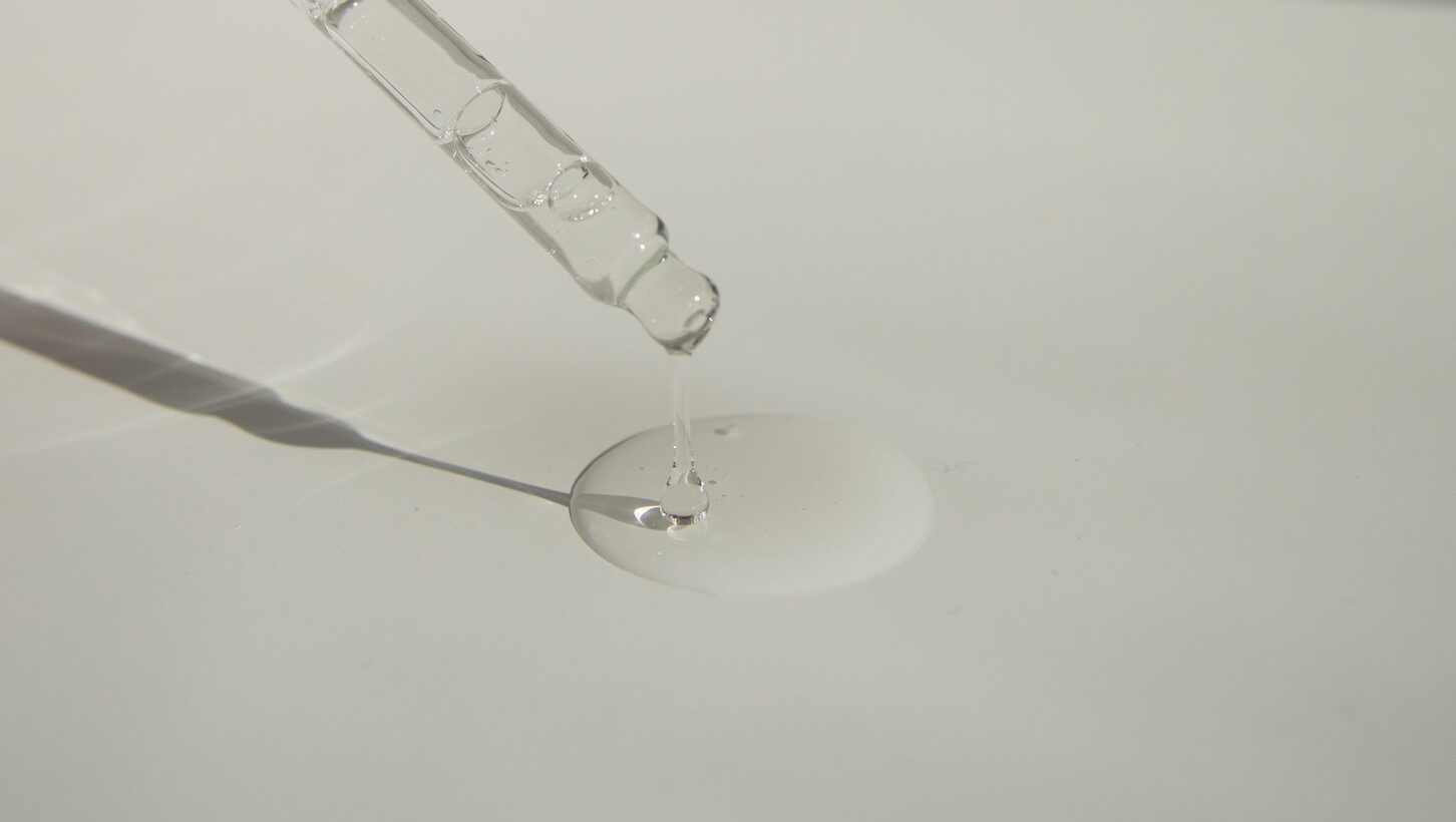 Anonymous person pouring liquid product on table with pipette