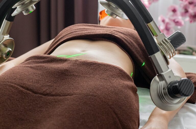 Crop anonymous female patient lying under lasers of fat loss machine on belly during treatment in light modern medical clinic